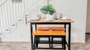 A dining area with a wooden table set for two, a potted plant, and a white staircase in the background. - 303/C Little Italy double balcony Loft /Parking (San Diego)