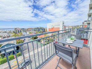 A balcony with a table set for two, overlooking a cityscape with buildings and a body of water. - 303/C Little Italy double balcony Loft /Parking (San Diego)