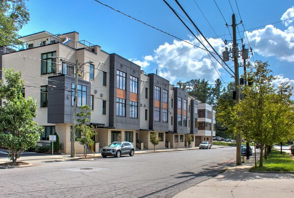 Un moderno edificio residencial de varios pisos con una combinación de balcones y ventanas, situado en una calle con coches aparcados y árboles.