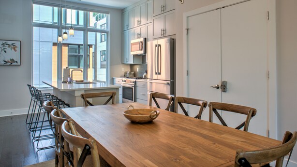 A modern kitchen with a wooden dining table, chairs, and a large window.
