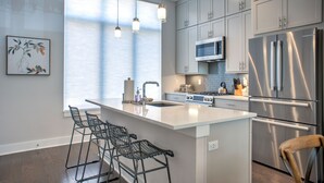A modern kitchen with a large island, bar stools, stainless steel appliances, and a view of the outdoors.