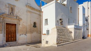 A narrow street with a white building featuring a wooden door and a stone wall. - GuestHost - Cute flat in the heart of Monopoli (Monopoli)