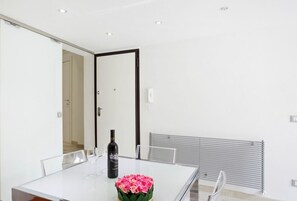 A modern dining area with a glass table, chairs, a bottle of wine, and a bouquet of flowers.