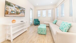 Una sala de estar moderna con un sofá blanco, un sillón azul verdoso y una consola blanca.