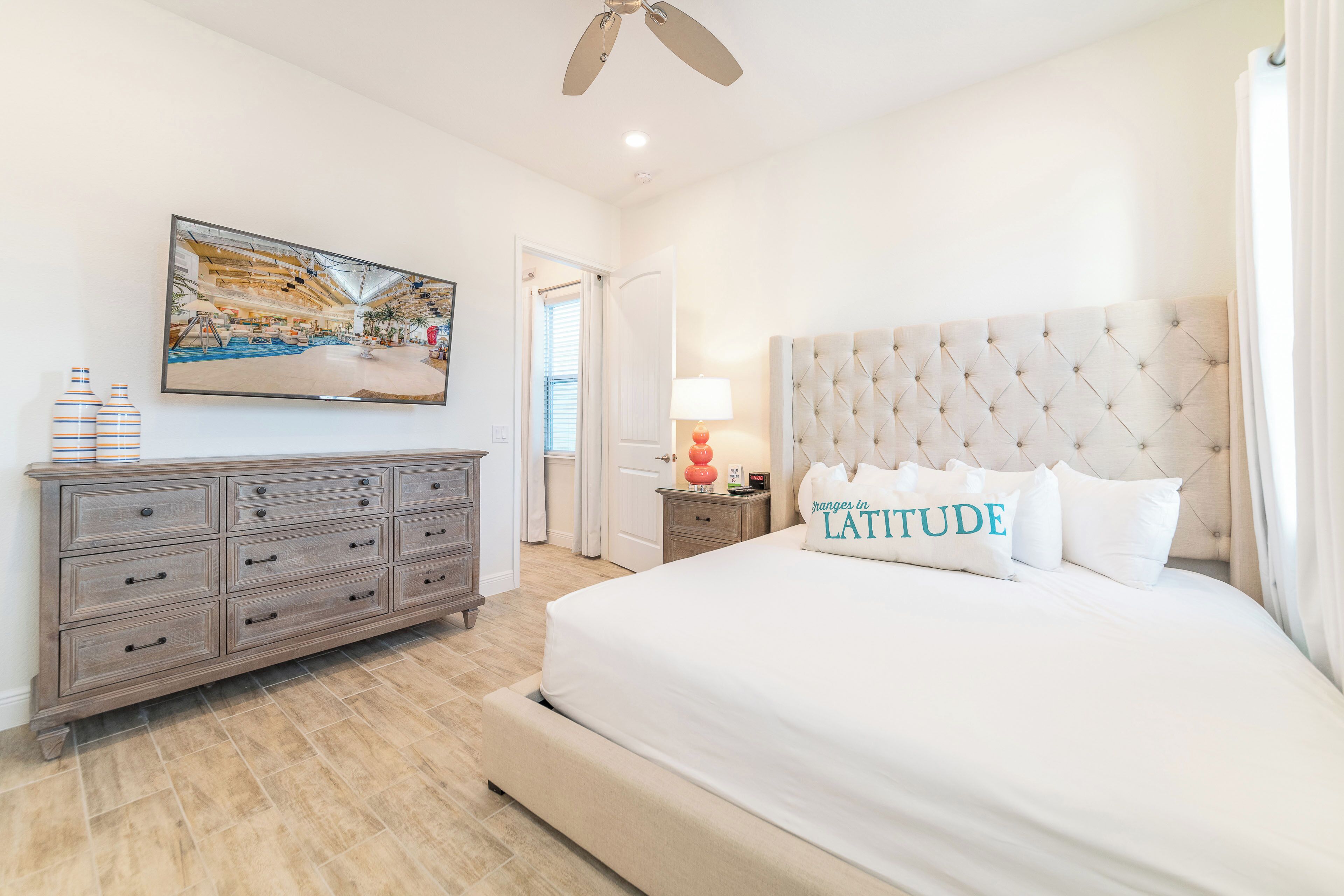 A bedroom with a large bed, a dresser, a television on the wall, and a ceiling fan.
