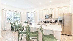 Una cocina moderna con armarios blancos, electrodomésticos de acero inoxidable y sillas verdes.