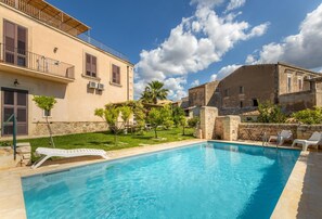 Una piscina con sillas de descanso, un muro de piedra y un edificio con balcón.
