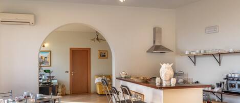 A spacious kitchen with a central island, a dining area with metal chairs, and a large arched doorway leading to another room.