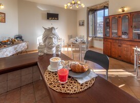 Un comedor con una mesa dispuesta para dos personas, mostrando un croissant, una taza de café y un vaso de bebida roja.