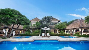 A pool area with two lounge chairs and a canopy, surrounded by thatched-roof structures and lush greenery. - Villa Pantai Karang (Denpasar)