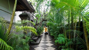 A checkered pathway flanked by lush greenery and a traditional building structure. - Villa Pantai Karang (Denpasar)