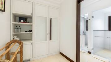 Una habitación con un armario blanco, una silla de madera y un baño visible a través de una puerta de cristal.