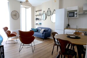 Un salon moderne avec un canapé bleu, des fauteuils rouges, une table à manger en bois et un coin cuisine équipé d’un four à micro-ondes.