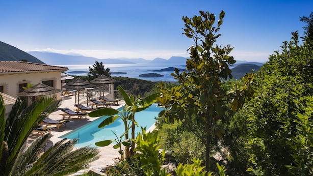A pool area with lounge chairs and umbrellas, surrounded by greenery and overlooking a scenic view of mountains and water. - Secluded THE VIEW Villa ideal for 10 adults & 7 kids w/t pool (Nidri)