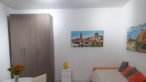 Een slaapkamer met een bed, een kledingkast, een klein tafeltje met een bloevas en twee schilderijen aan de muur.