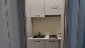 Een smalle gang die uitkomt in een kleine keuken met witte kastjes, een spoelbak en een fornuis.