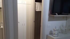 Een kamer met een kledingkast, een televisie op een plank en een toiletrolhouder.