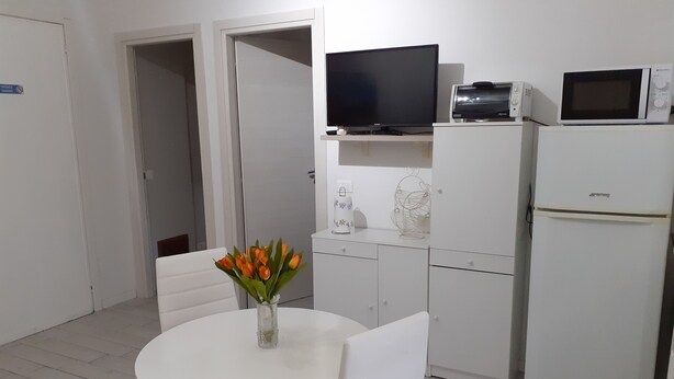 Een kleine, schone kamer met witte meubels, een televisie, een magnetron en een koelkast.