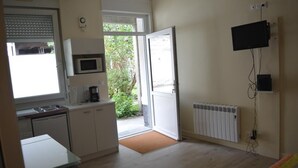 A compact kitchen with a microwave, coffee maker, and a small table. A sliding door leads to a garden area.