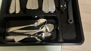 A black tray with various cutlery including spoons, forks, knives, and a pair of tongs.