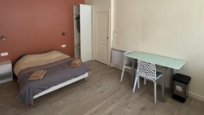 A bedroom with a bed, a desk, a radiator, and a trash bin.