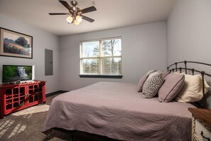 A bedroom with a bed, a TV on a red cabinet, a ceiling fan, and a window with blinds.