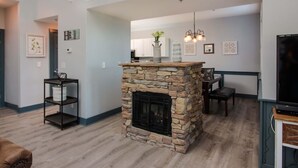 A living room with a stone fireplace, wooden flooring, a dining area with a table and chairs, and a television on a stand. - 3206 Golf View Hillcrest The Clubhouse (Pigeon Forge)