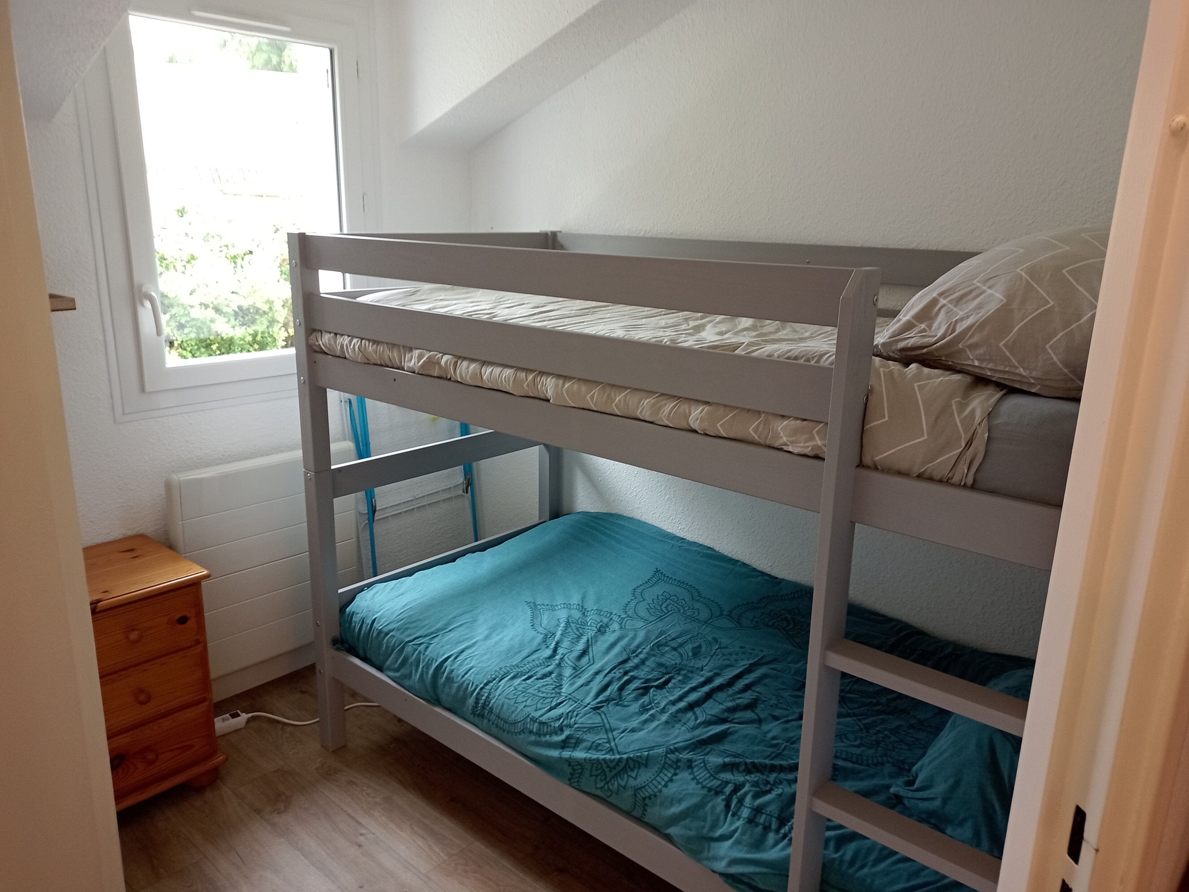 A bunk bed with a window above, a wooden dresser, and a radiator on the wall.