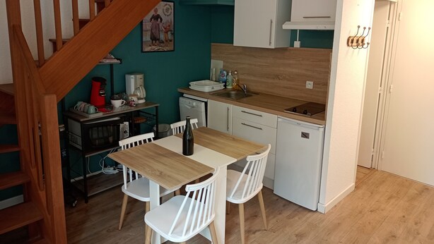 Uma cozinha compacta com uma mesa e cadeiras de madeira, cafeteira e máquina de lavar louça.