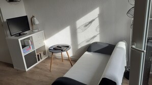 Uma sala de estar moderna com um sofá, uma mesinha lateral, uma televisão sobre um móvel branco e uma parede com textura.
