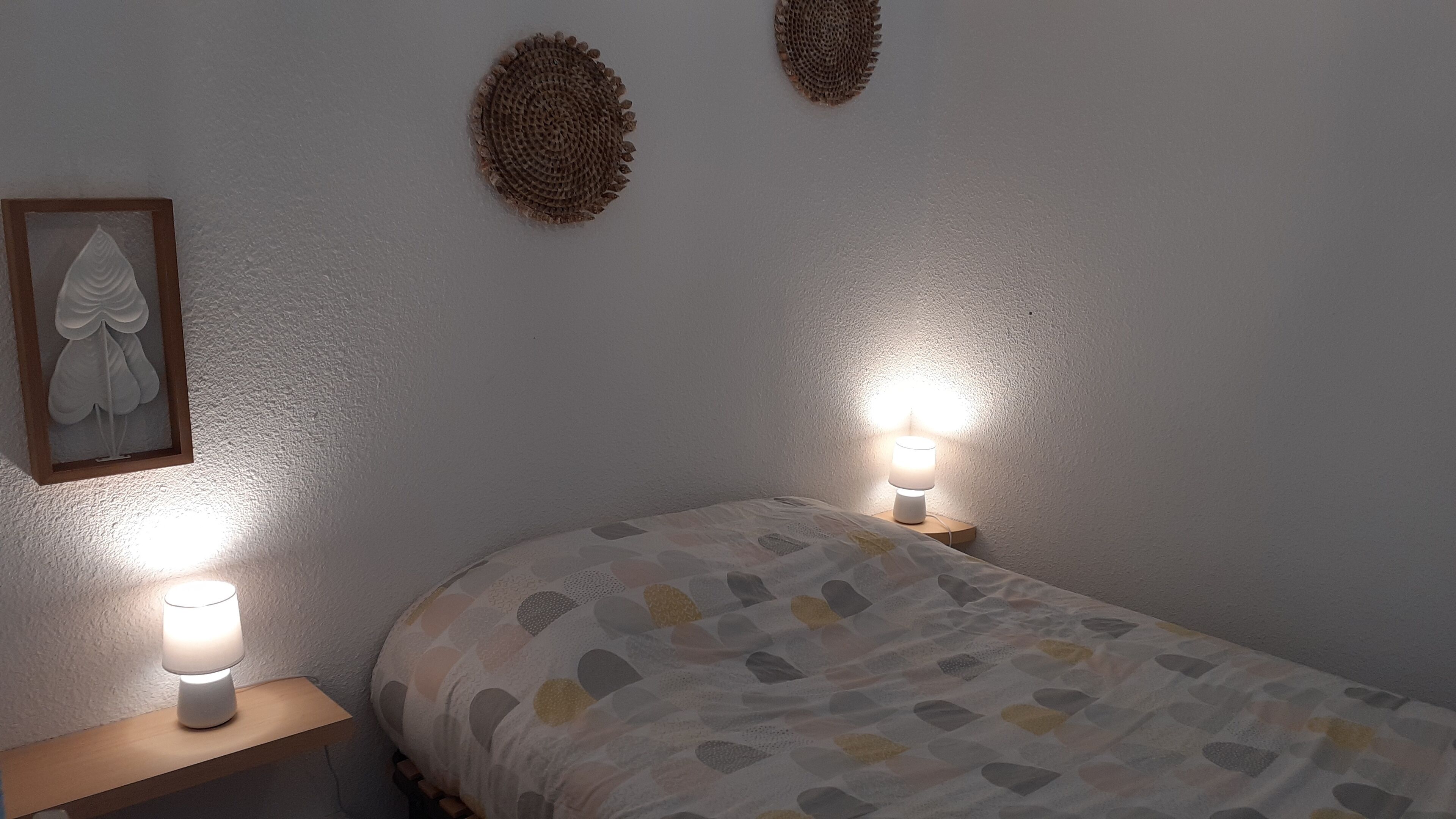 Un dormitorio con una cama, dos lámparas de noche, una obra de arte enmarcada y dos adornos de pared.