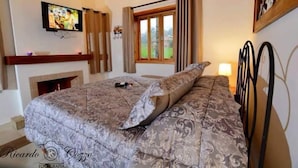 Quarto com uma cama grande, televisão na parede, lareira e janela com cortinas.