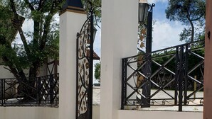 Um caminho de pedra leva a um portão com grade de metal e pilares decorativos.