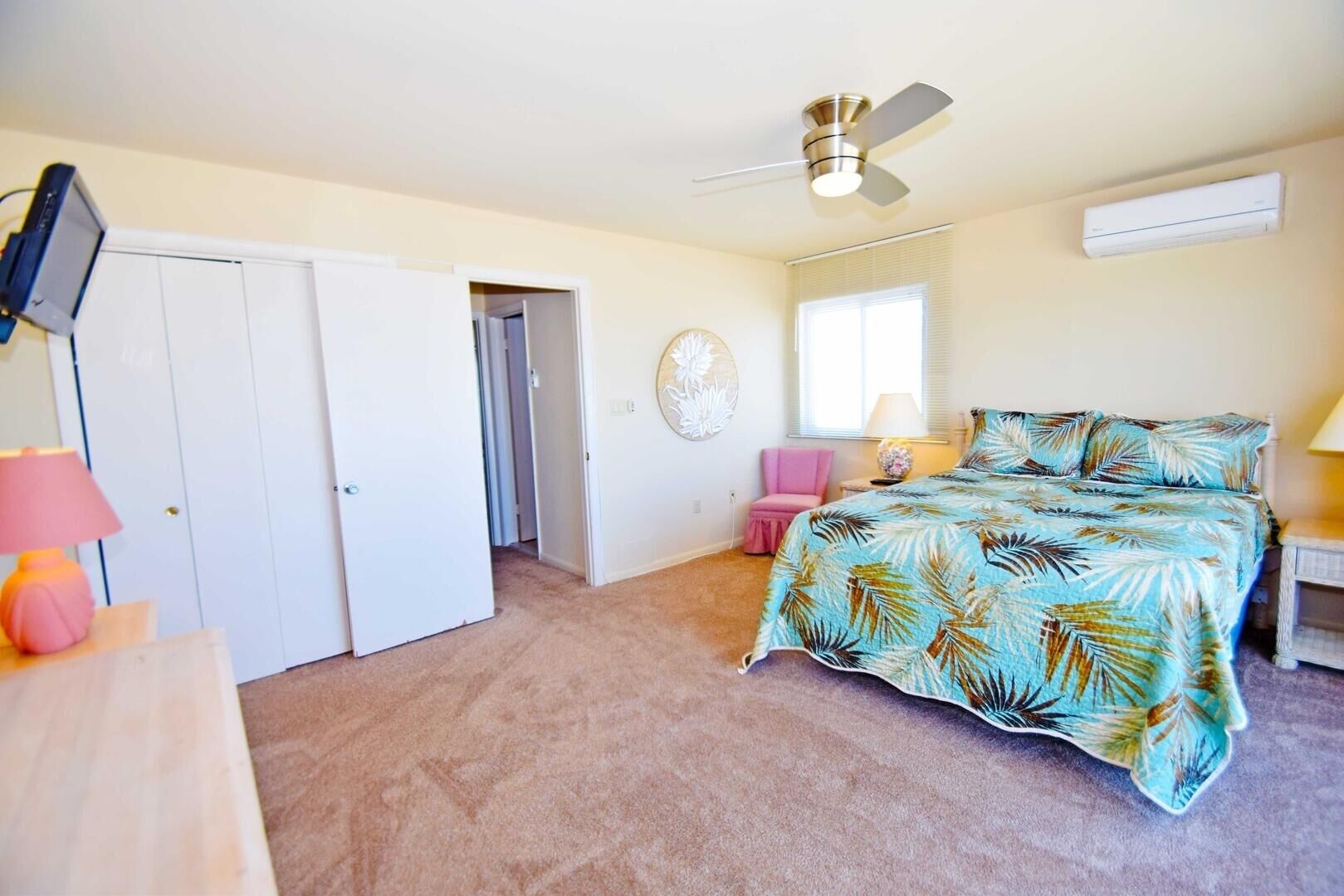 A bedroom with a bed, a ceiling fan, a window with blinds, a door, and a wall-mounted air conditioner.