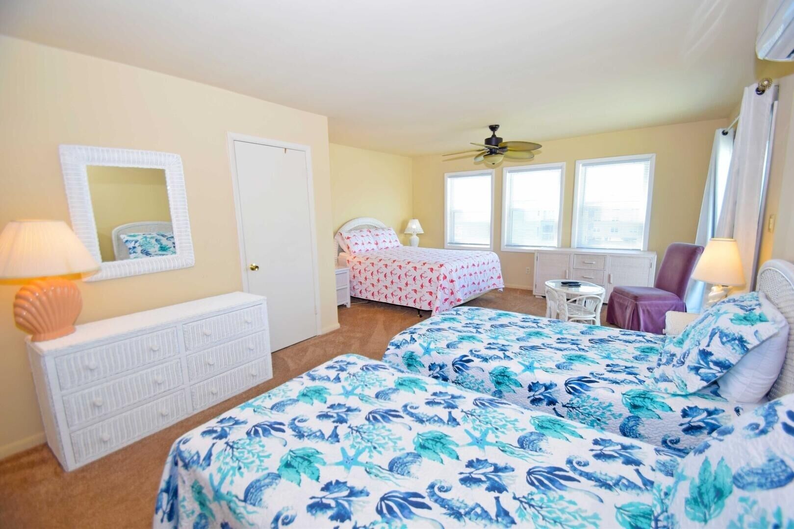 A bedroom with two beds, a dresser, a chair, a small table, and a ceiling fan.