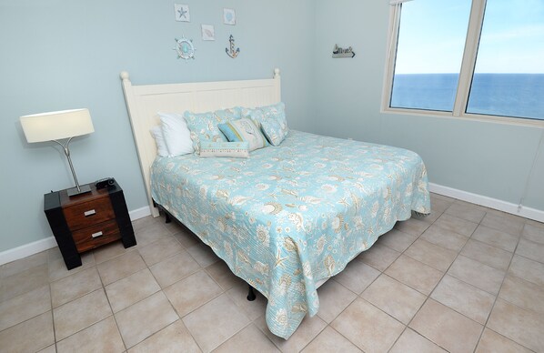 Un dormitorio con cama, mesita de noche, lámpara y vistas al mar a través de una ventana.
