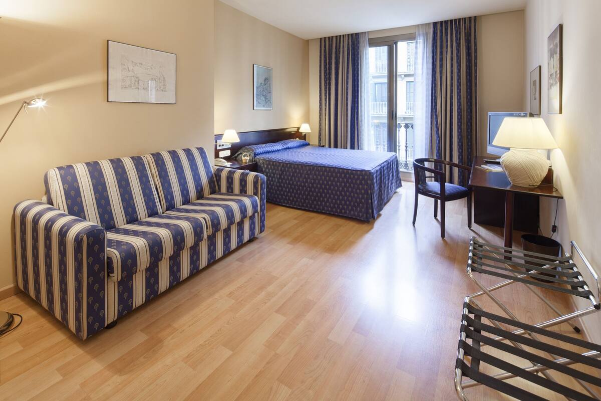 A hotel room with a bed, a sofa, a desk, and a chair.
