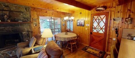 LâintĂ©rieur dâun chalet chaleureux, avec une cheminĂ©e en pierre, des canapĂ©s en cuir, une table Ă manger et une porte en bois ornĂ©e dâune croix.