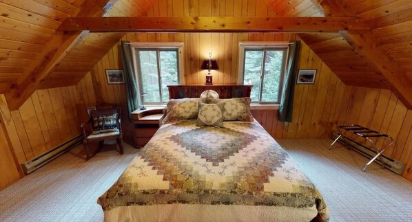 A cozy attic bedroom with a large bed, two windows, a desk, and a chair.