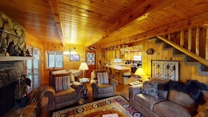 L’intérieur d’un chalet en bois chaleureux et accueillant, avec une cheminée, des canapés en cuir, un coin repas et un escalier.