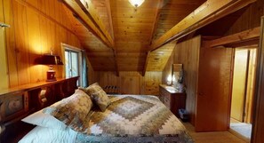 Een slaapkamer in een houten hutje, met een bed, een dressoir en een raam.