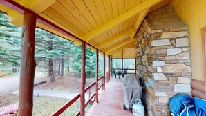Un espace extérieur abrité, doté d’une cheminée en pierre, d’un barbecue et offrant une vue sur la forêt environnante.