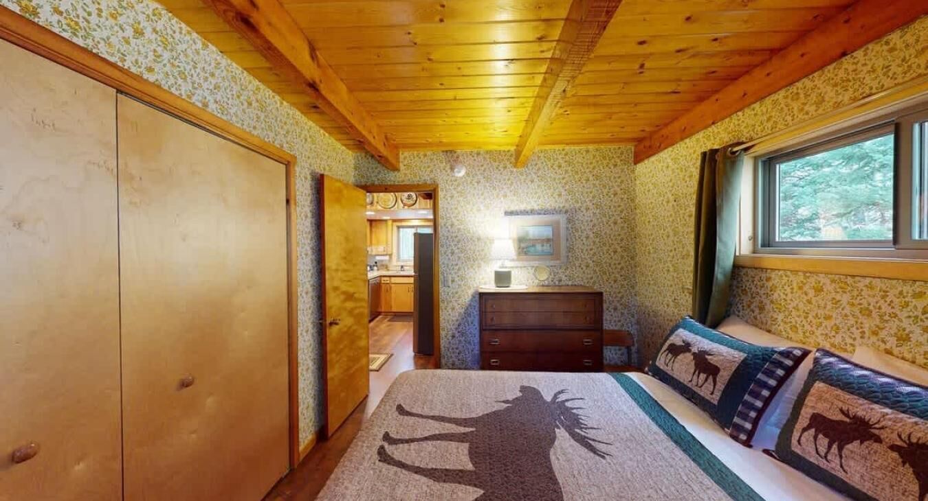 Una habitación con una cama, un tocador, una ventana y una puerta que da a otra habitación.
