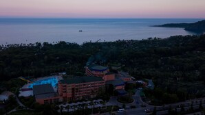 A resort with a swimming pool, a large building with multiple floors, and a view of the sea. - Simena Comfort Hotel (Kemer)