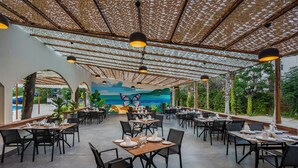 An outdoor dining area with tables and chairs, a mural on the wall, and a view of the outdoors. - Simena Comfort Hotel (Kemer)