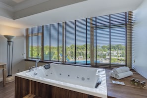 A modern bathroom with a large bathtub, wooden flooring, and a view of a swimming pool through large windows. - Simena Comfort Hotel (Kemer)