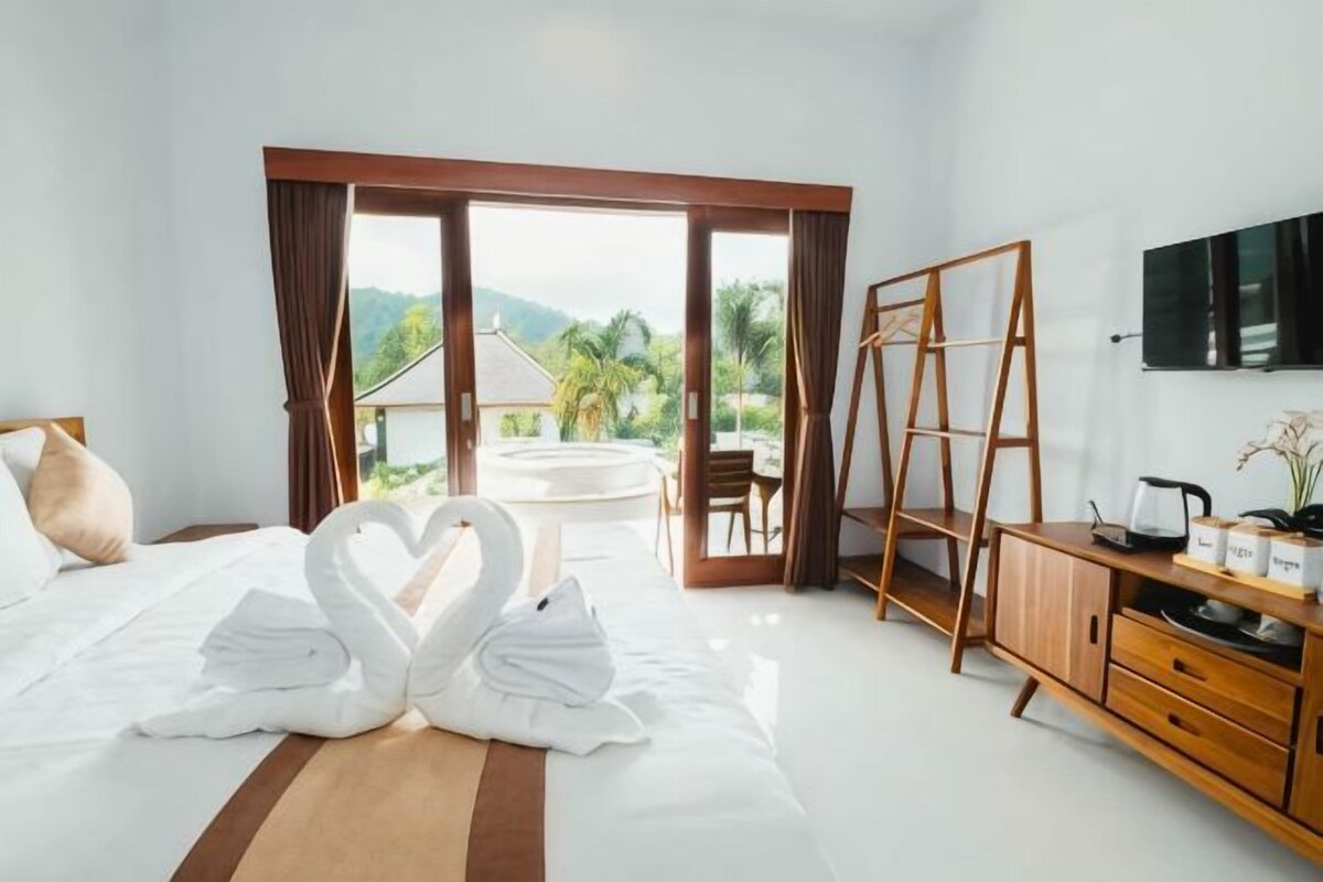 A hotel room with a bed, a wooden desk, a TV, and a view of the outdoors.