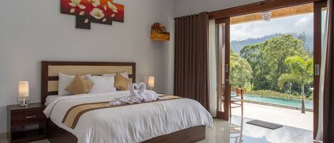 Habitación de hotel con una cama grande, una mesita de noche, una lámpara, un cuadro y vistas a una piscina y vegetación.