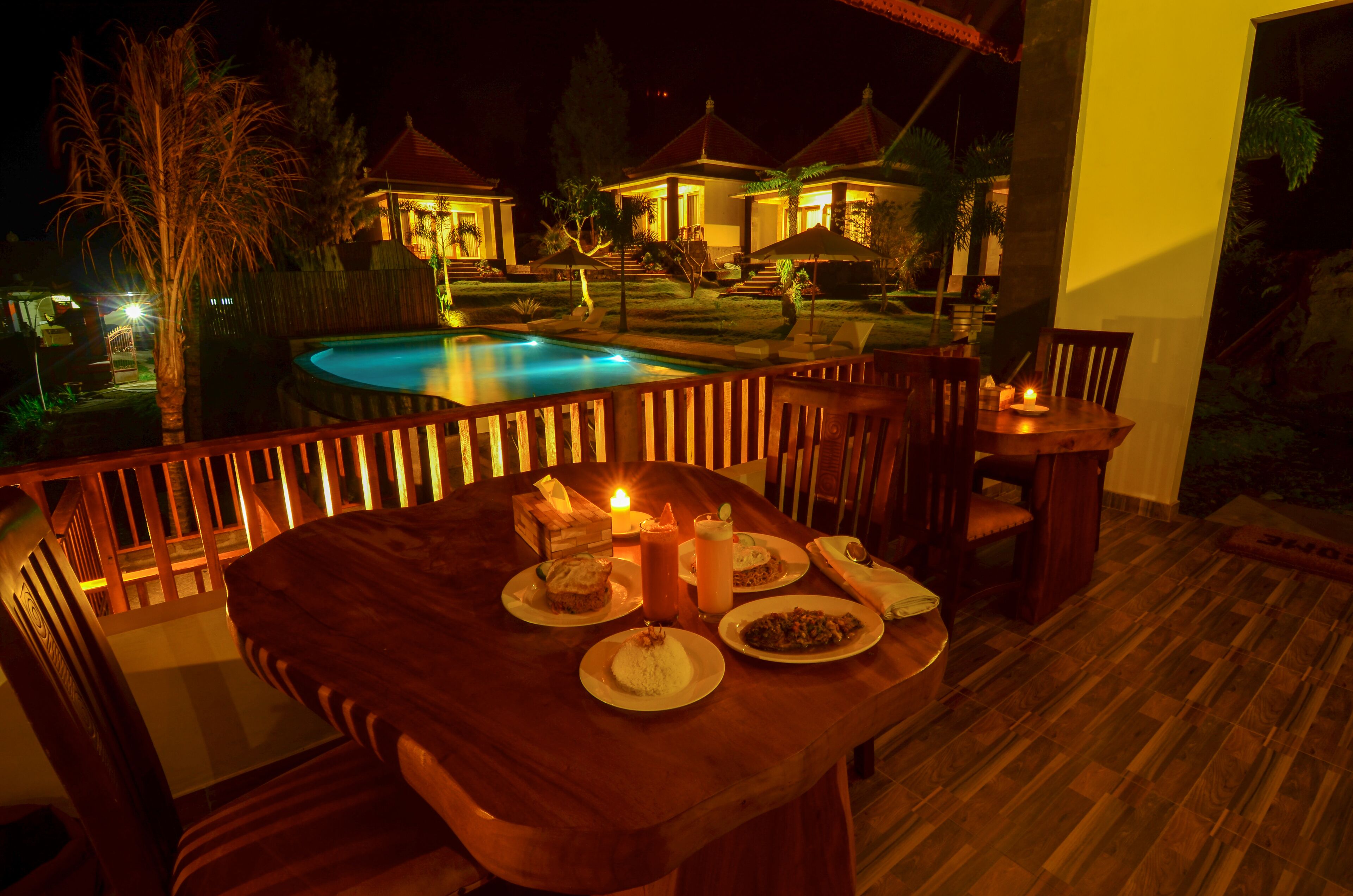 Ein Essbereich mit Blick auf einen Pool, Holzmöbel und einem Tisch mit Kerzen.