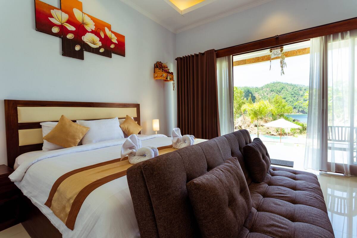 A hotel room with a bed, a sofa, a view of the outdoors, and a painting on the wall.
